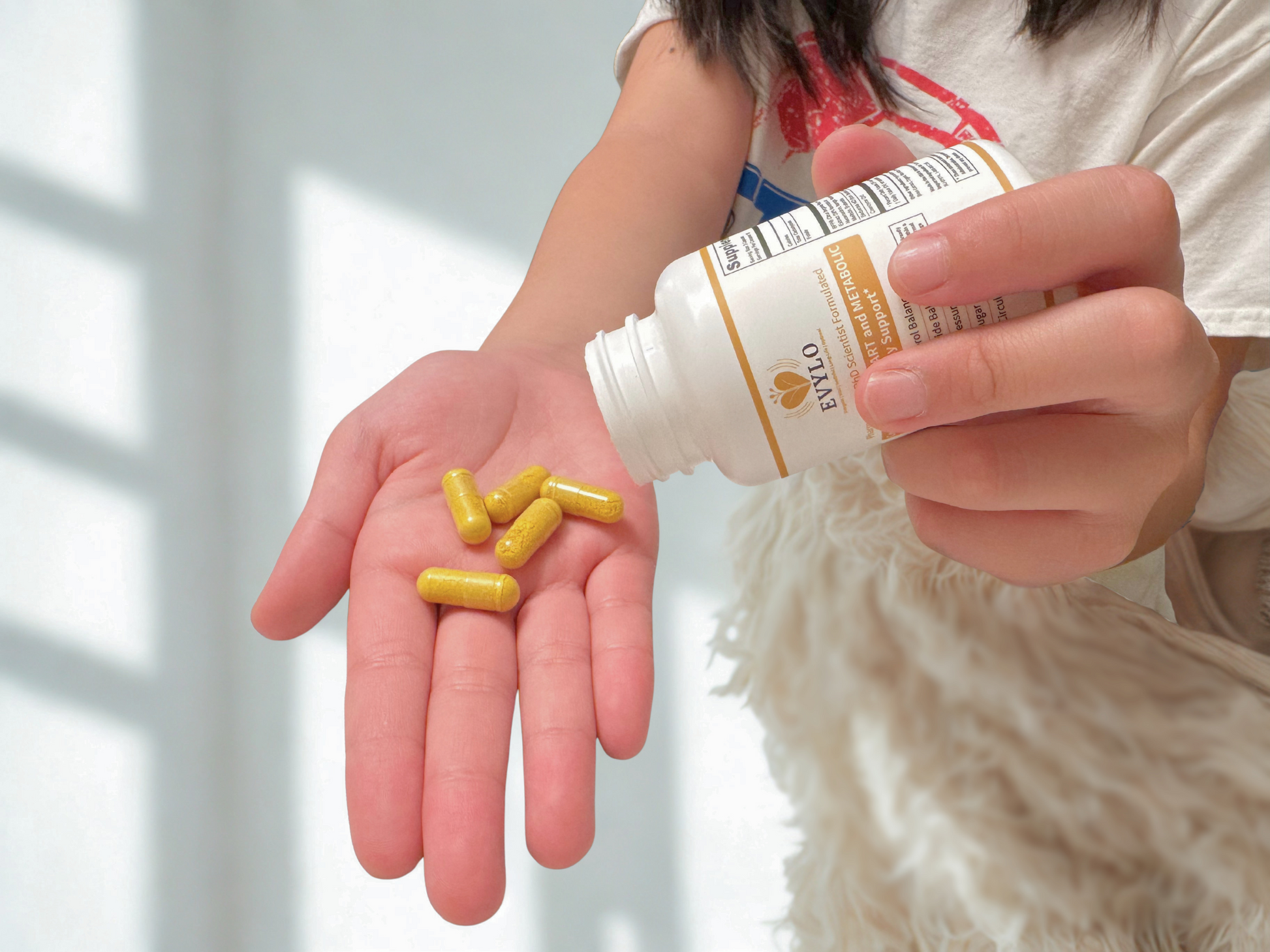 Hand holding EVYLO heart health supplement capsules from bottle, daily support for healthy cholesterol, triglyceride, blood sugar, blood pressure, and circulation.